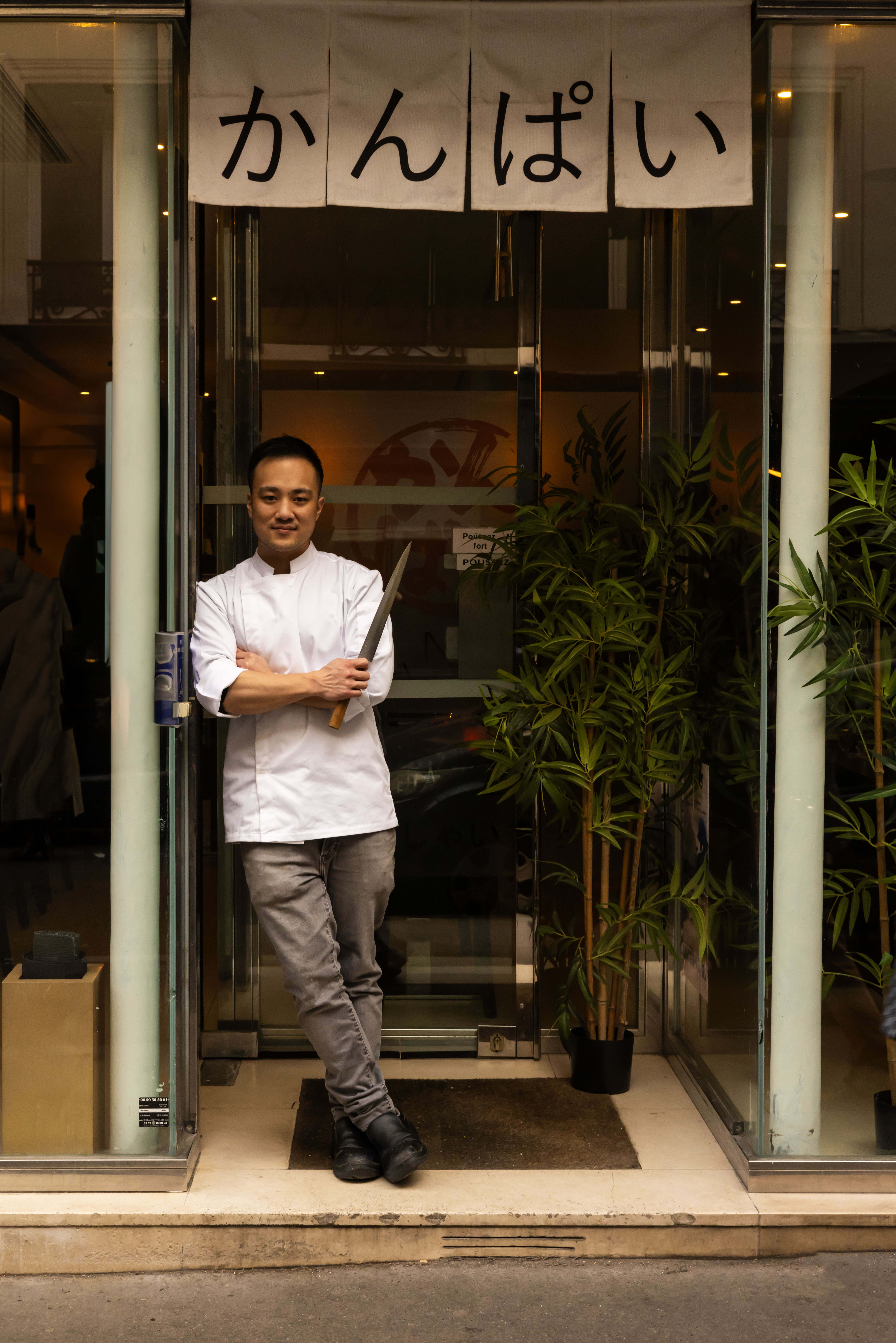 Le chef de Kanpai Paris devant l'entrée du restaurant, couteau yanagiba à la main